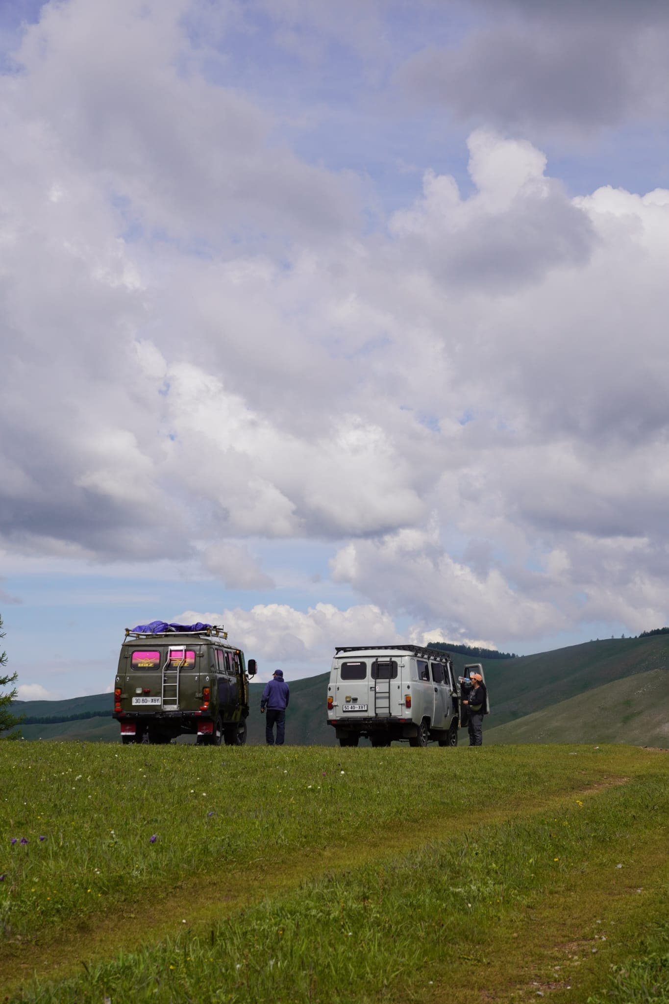 Two expedition vehicles parked on the open Mongolian grassland under a big sky