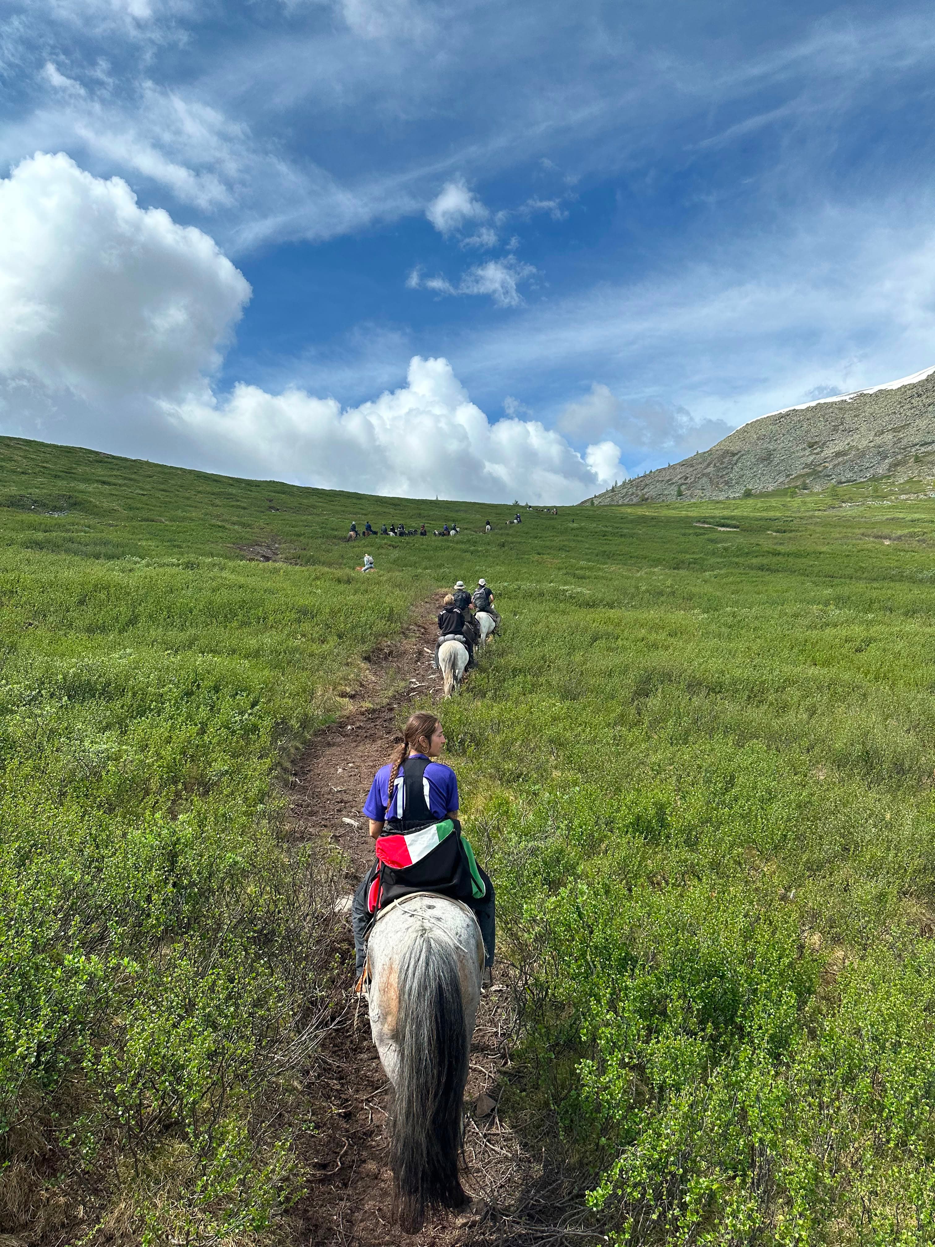 A line of riders on horseback crossing a green valley in Mongolia