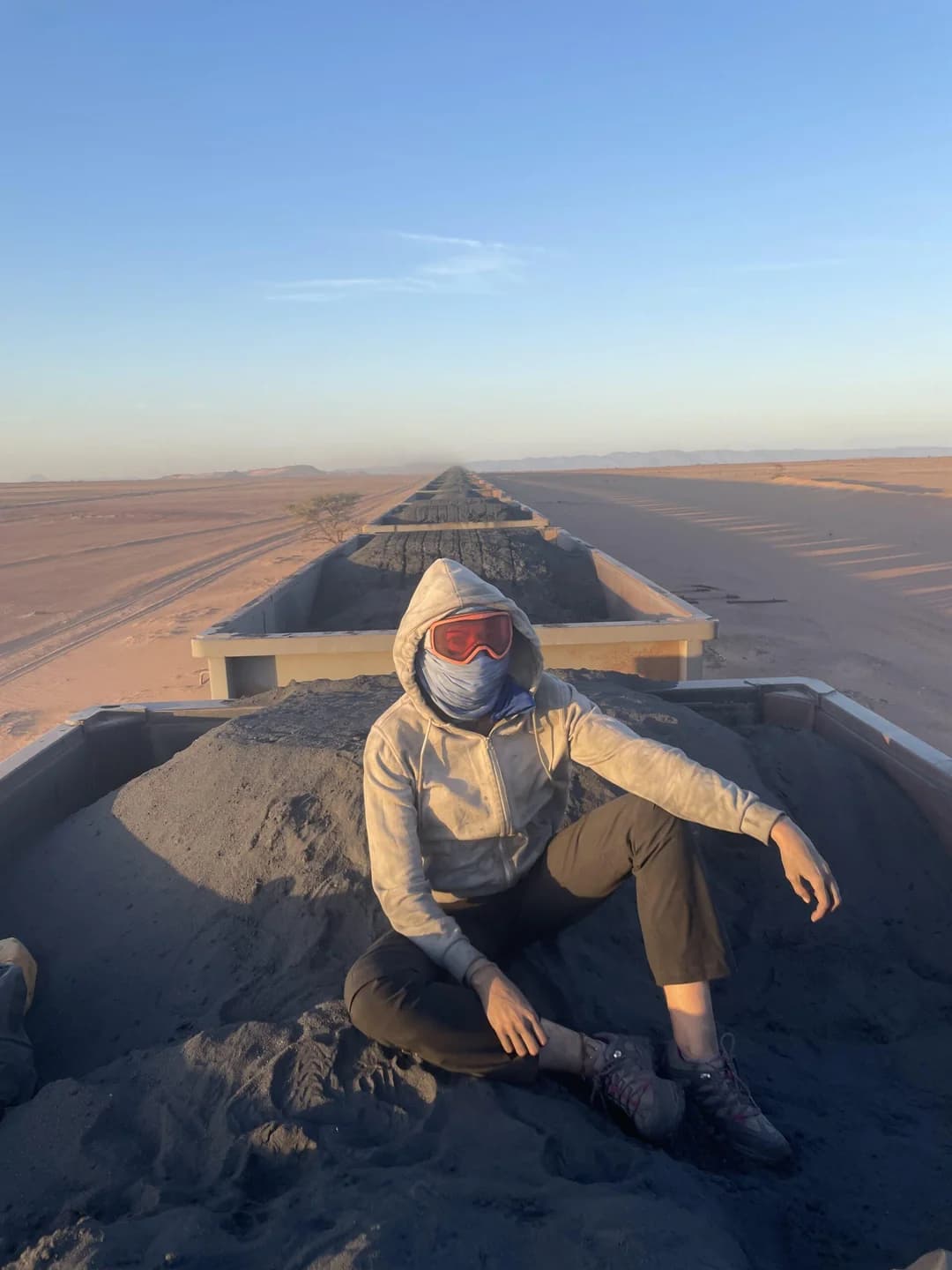 A traveller wrapped against the wind and dust, riding on top of the Mauritania iron ore train through the desert