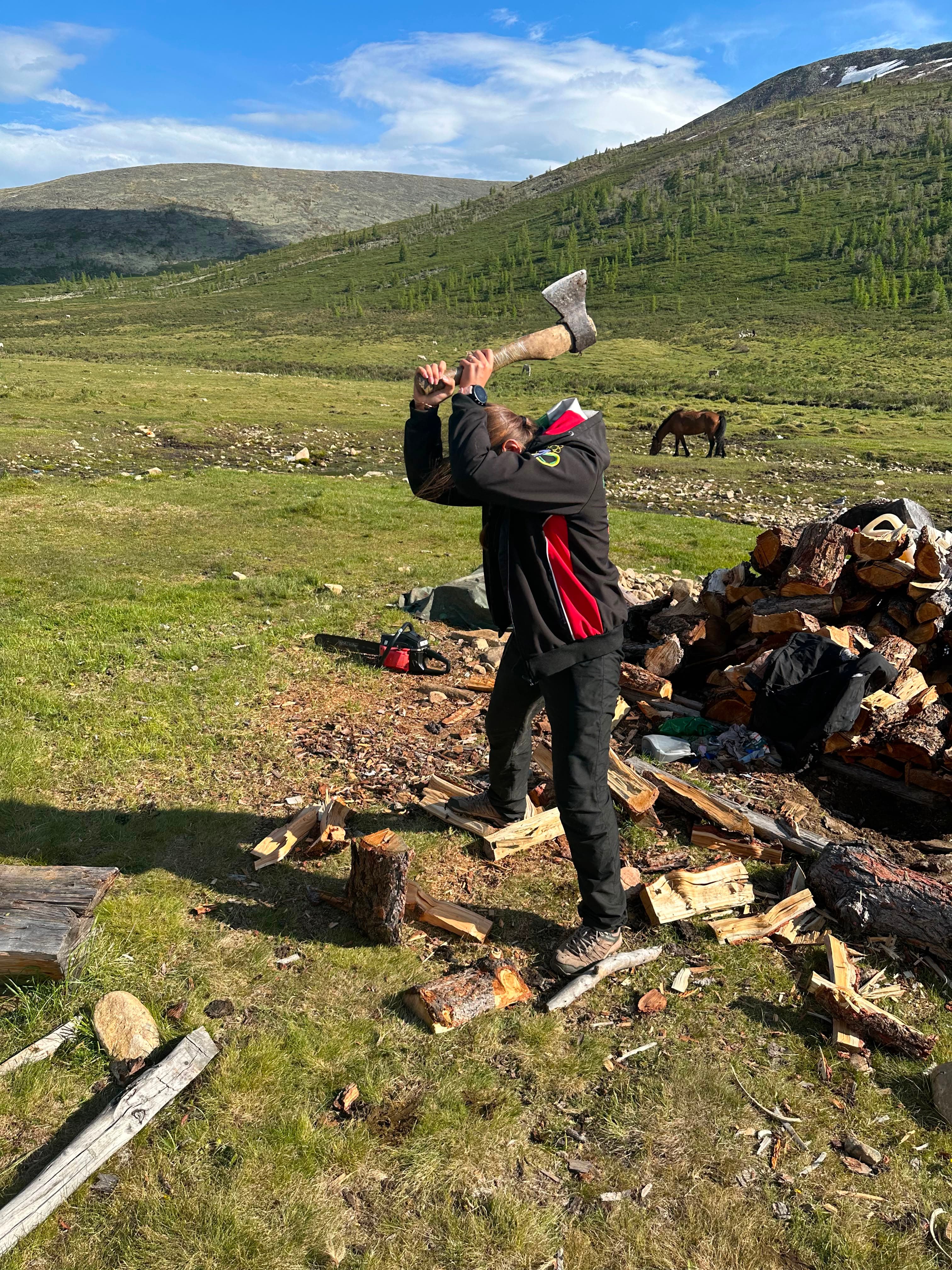 An expedition traveller chopping firewood at camp, mountains in the background — the kind of unposed, hands-on moment these trips are built around