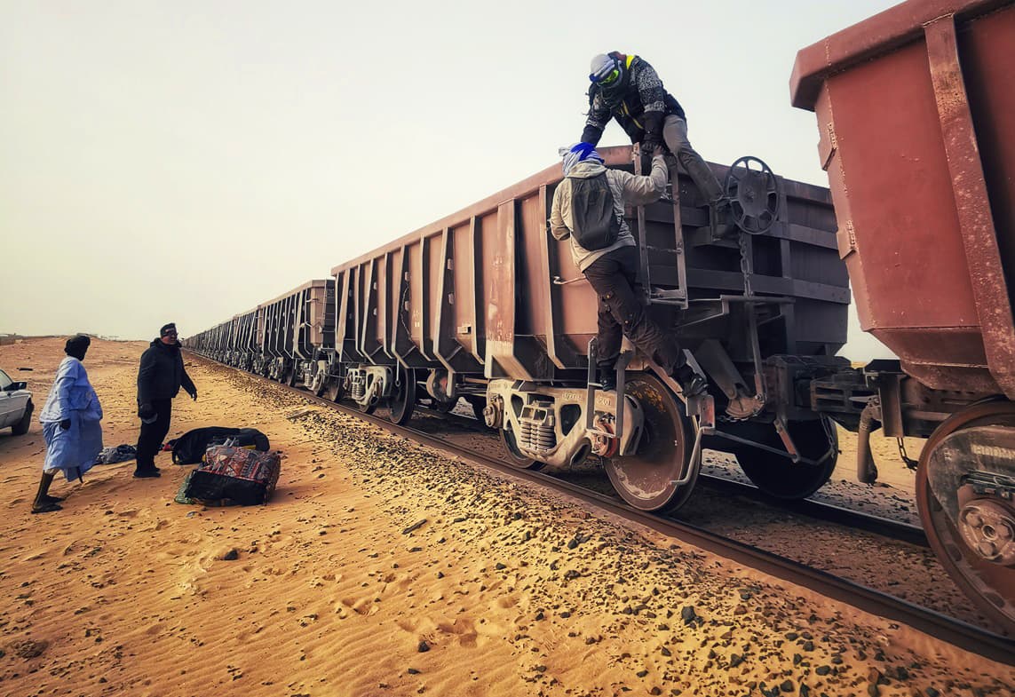 Travellers climbing onto a wagon of the Mauritania iron ore train in the desert