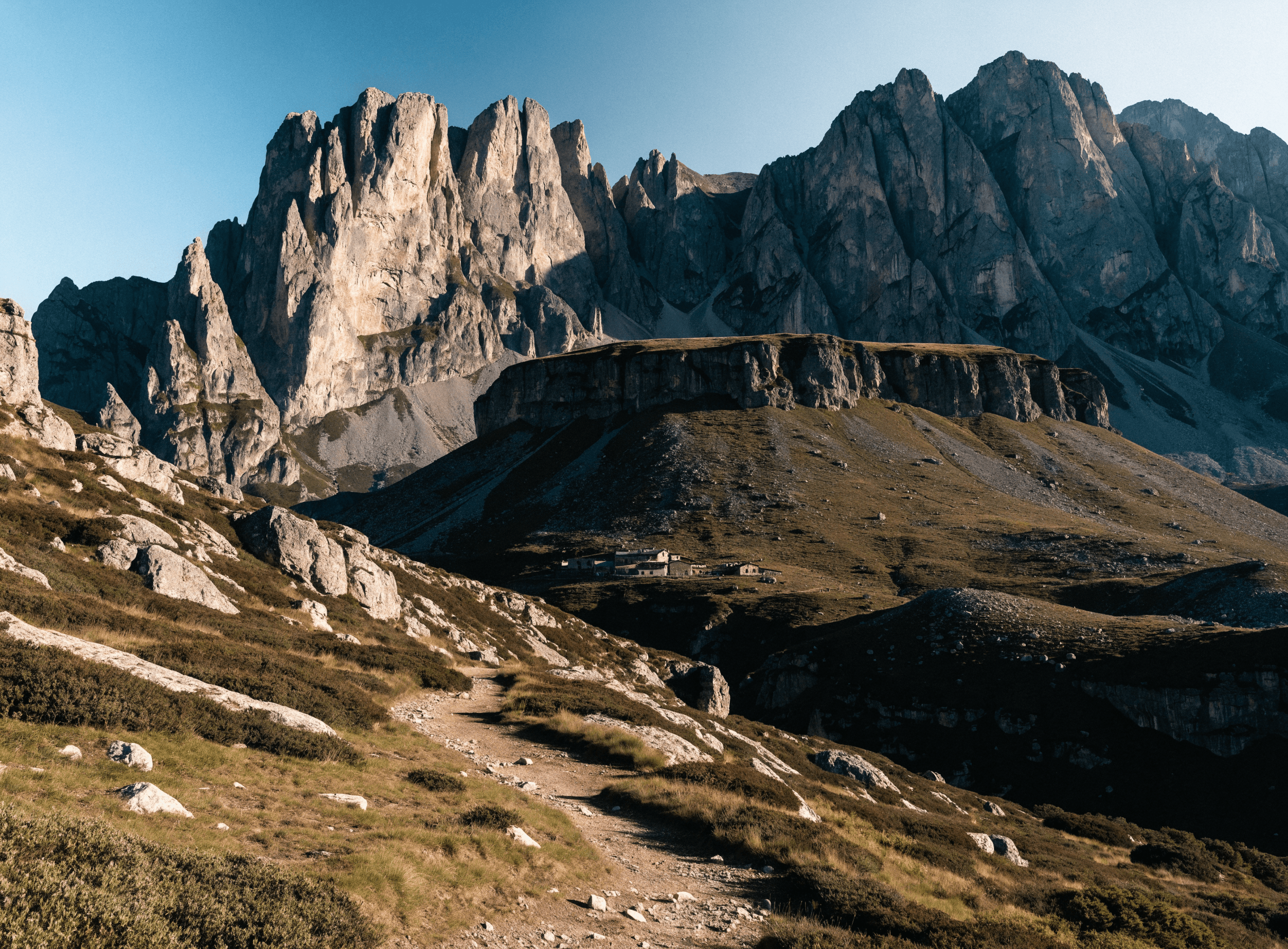 The jagged peaks of the Gran Sasso mountain range in Abruzzo, Italy, with a hiking trail and a small mountain refuge below